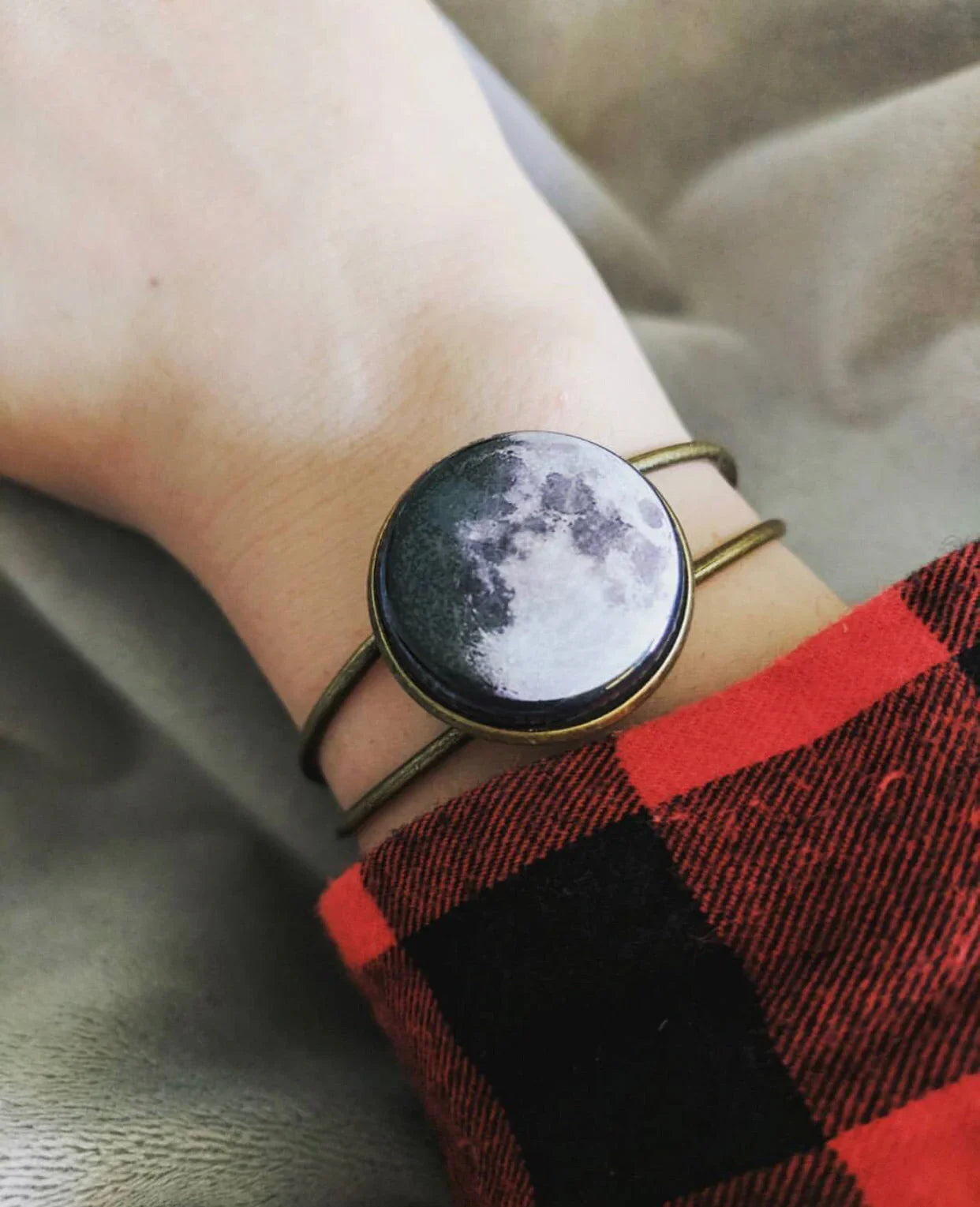 Moon phase bracelet with brass band worn on wrist over red and black checkered shirt