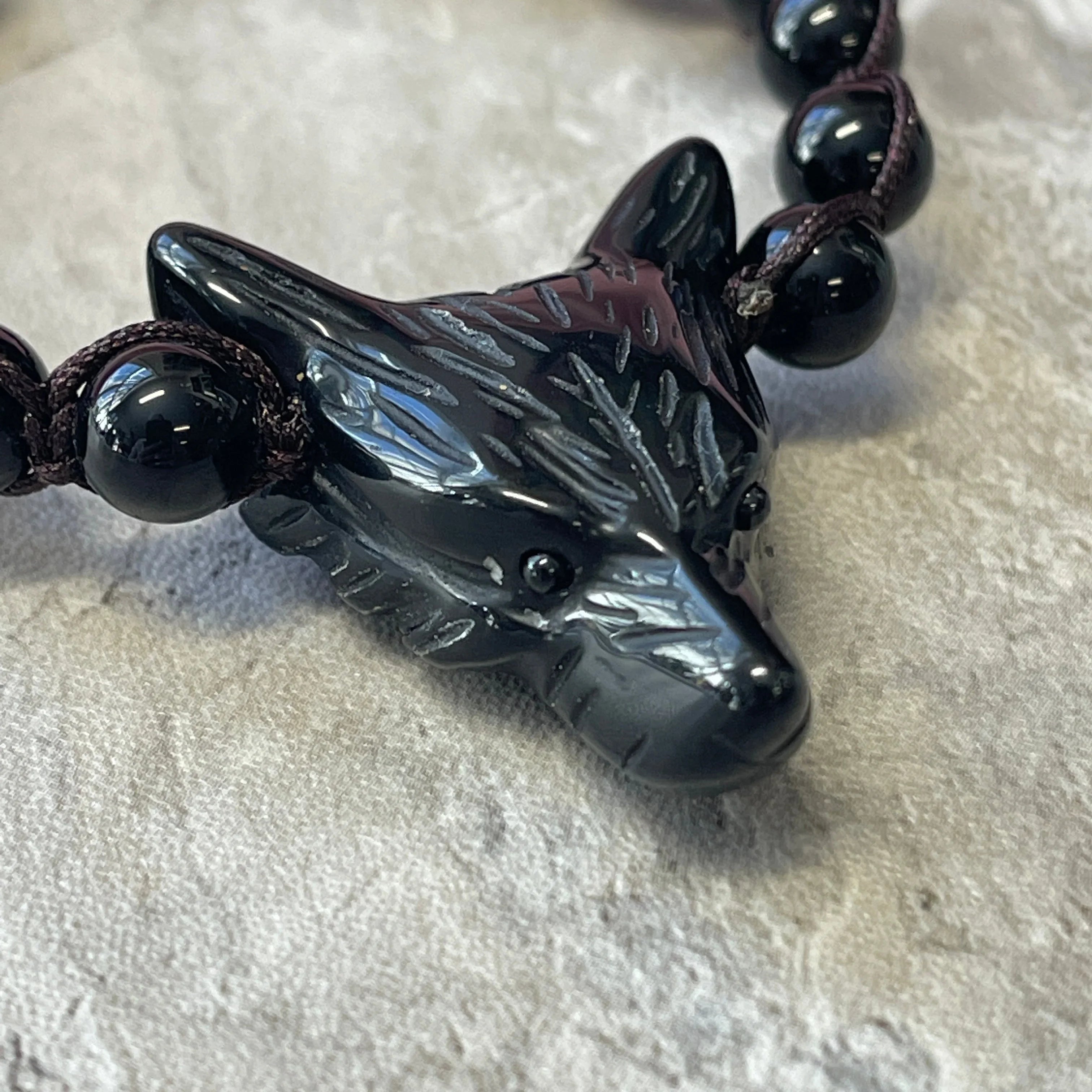 Black wolf head gemstone bracelet with round beads on textured grey surface at Qu!rk Boutique