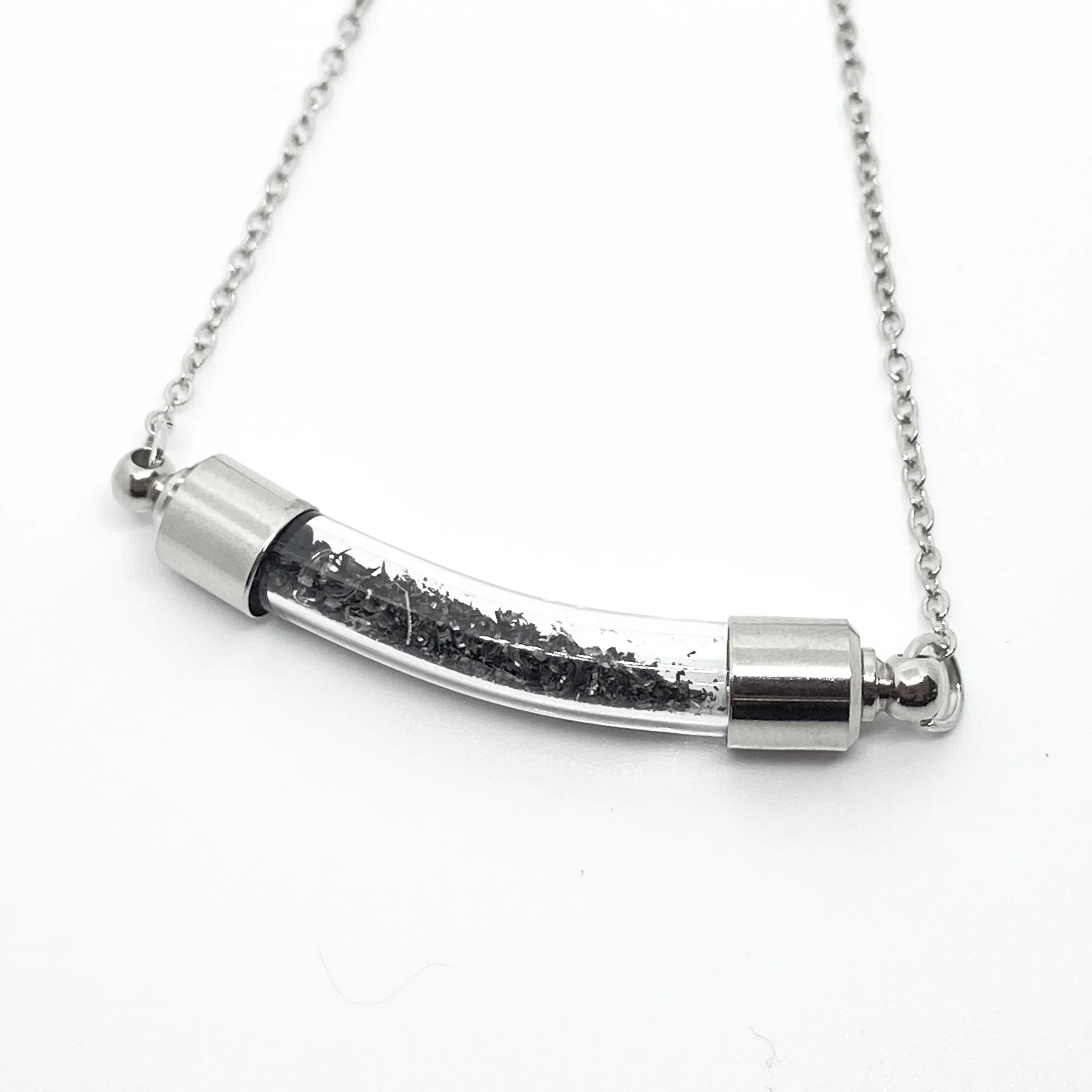 silver chain necklace with curved glass pendant containing black particles