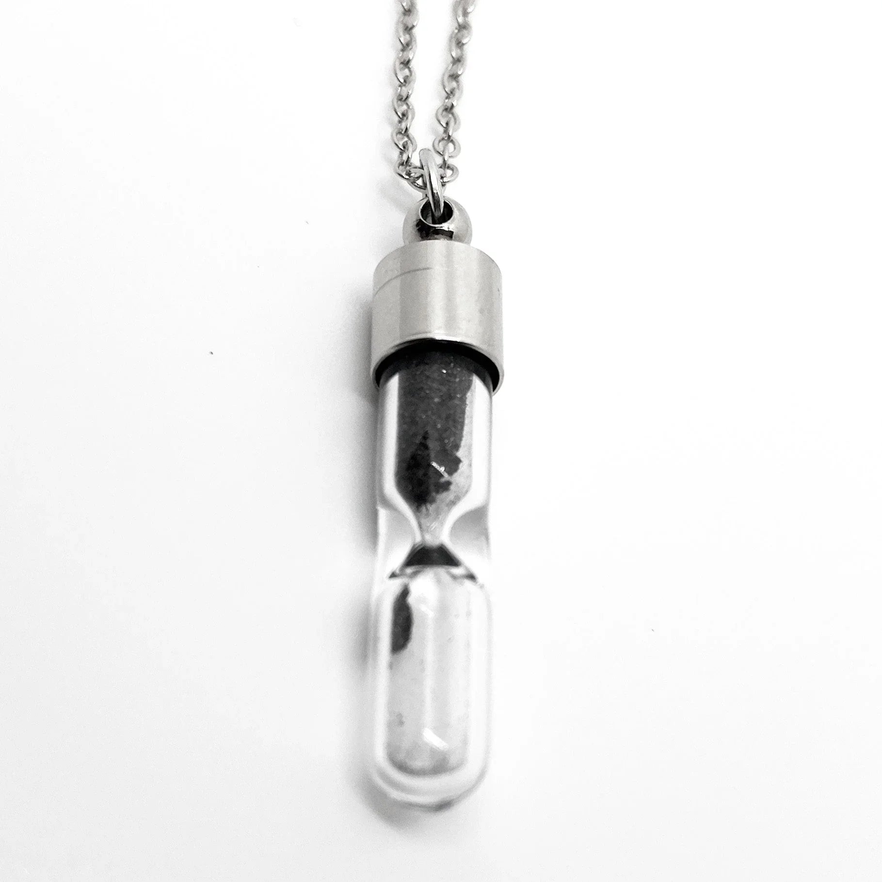 Silver hourglass pendant necklace with black sand on white background