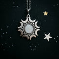 Silver moon phase pendant with central moonstone on chain against a starry black background