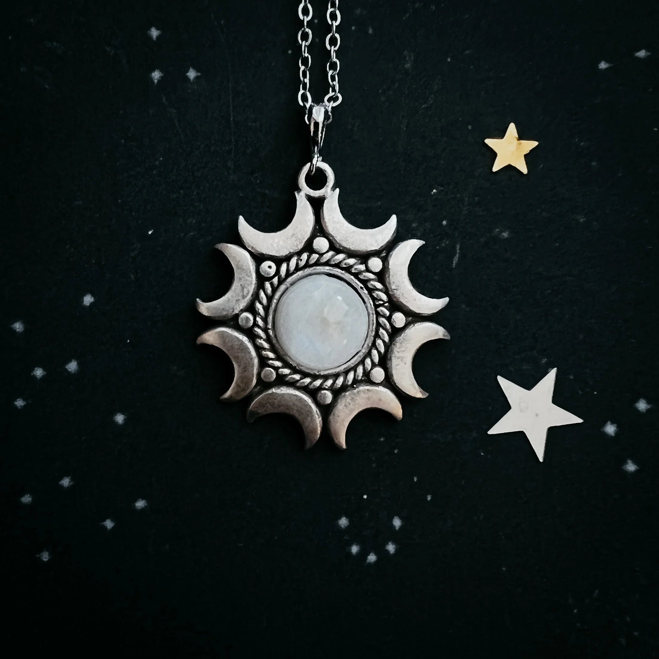 Silver moon phase pendant with central moonstone on chain against a starry black background