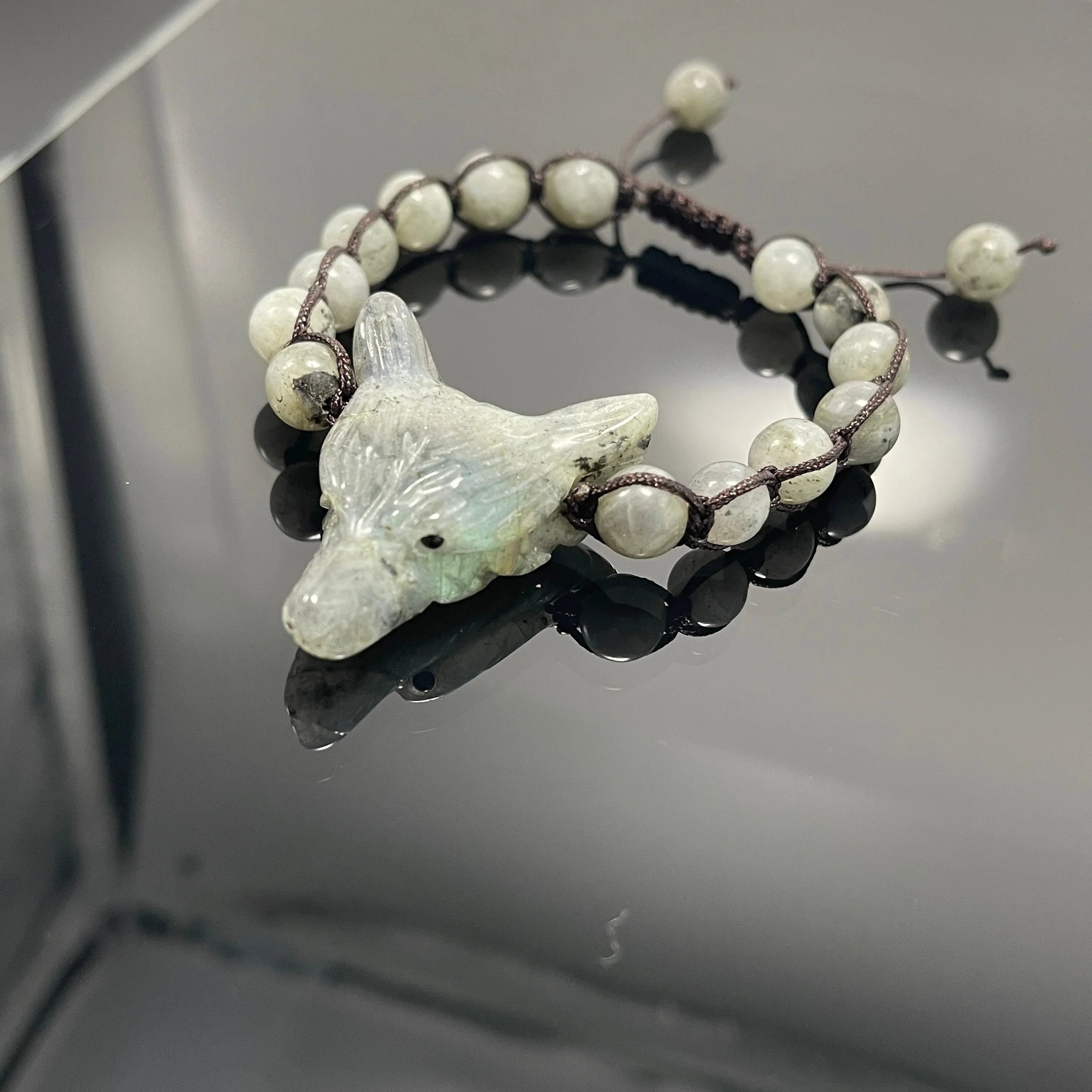 Handmade wolf head gemstone bracelet with round beads on black reflective surface at Qu!rk Boutique