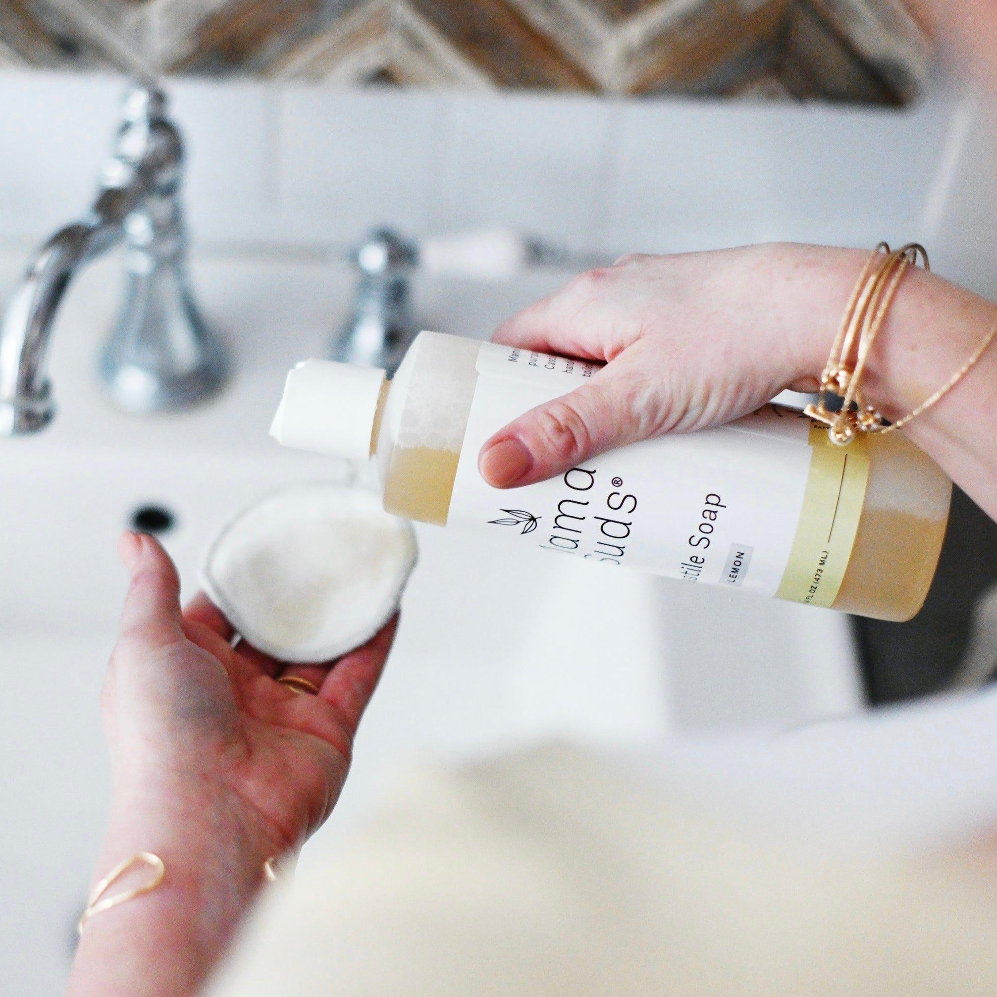 Woman pouring MamaSuds liquid soap onto a reusable pad at a modern sink.