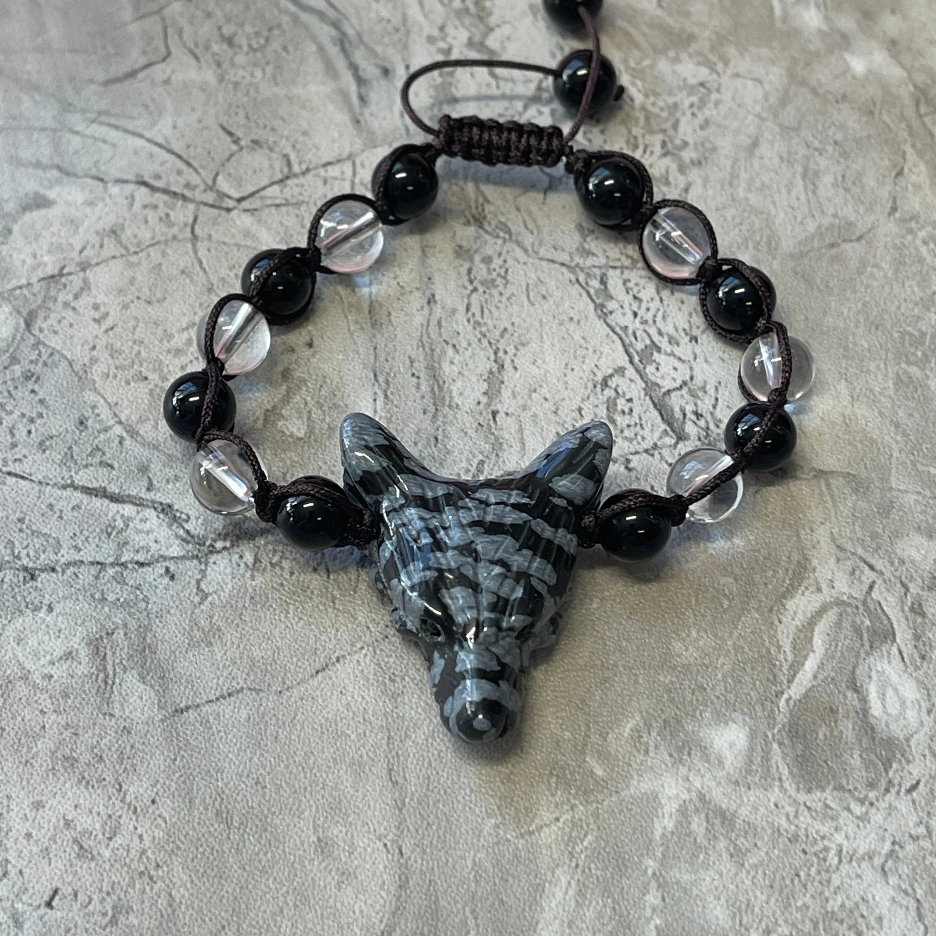 Black and clear beaded bracelet with carved wolf head centerpiece on gray stone background