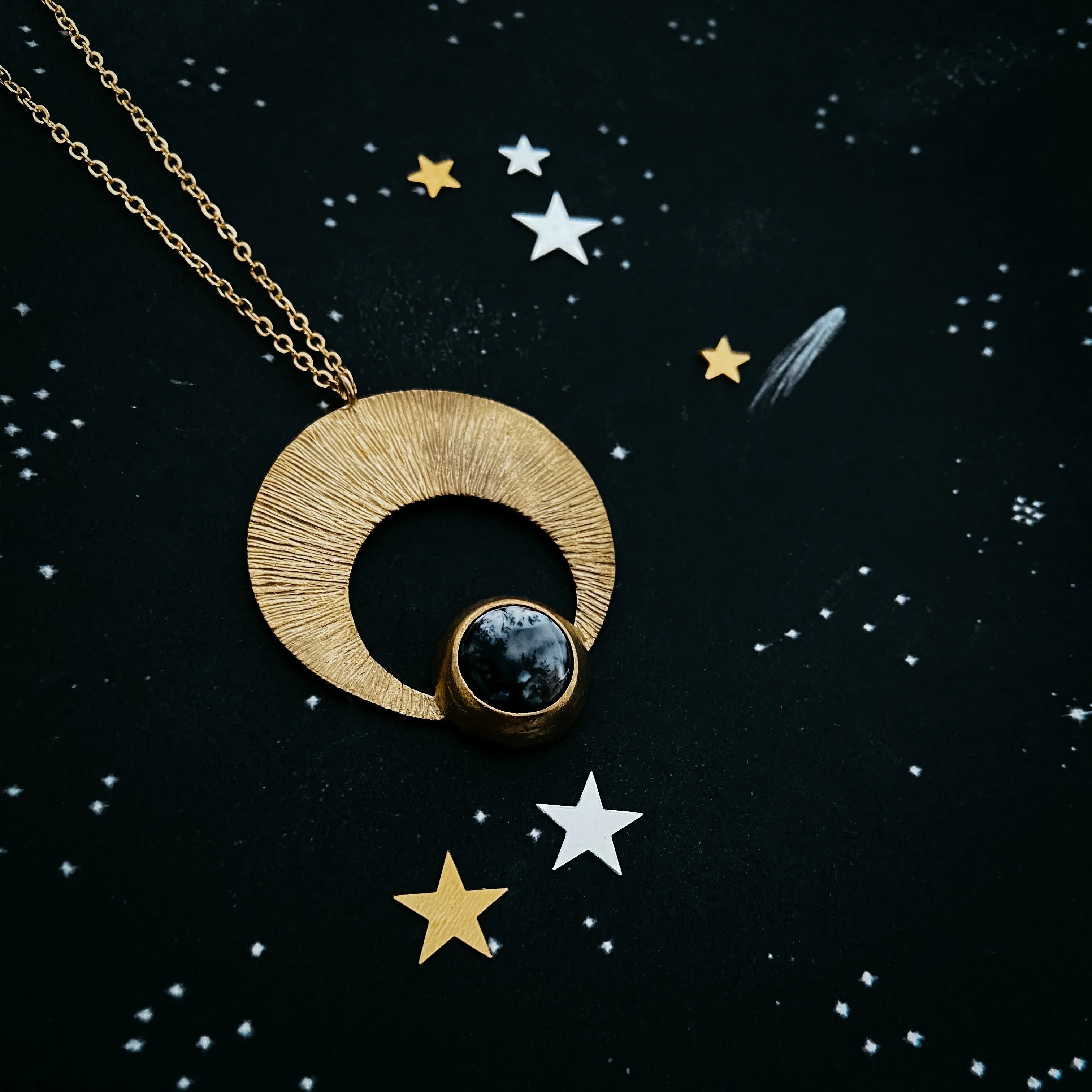 Gold crescent moon necklace with black gemstone on cosmic star background, Qu!rk Boutique jewelry