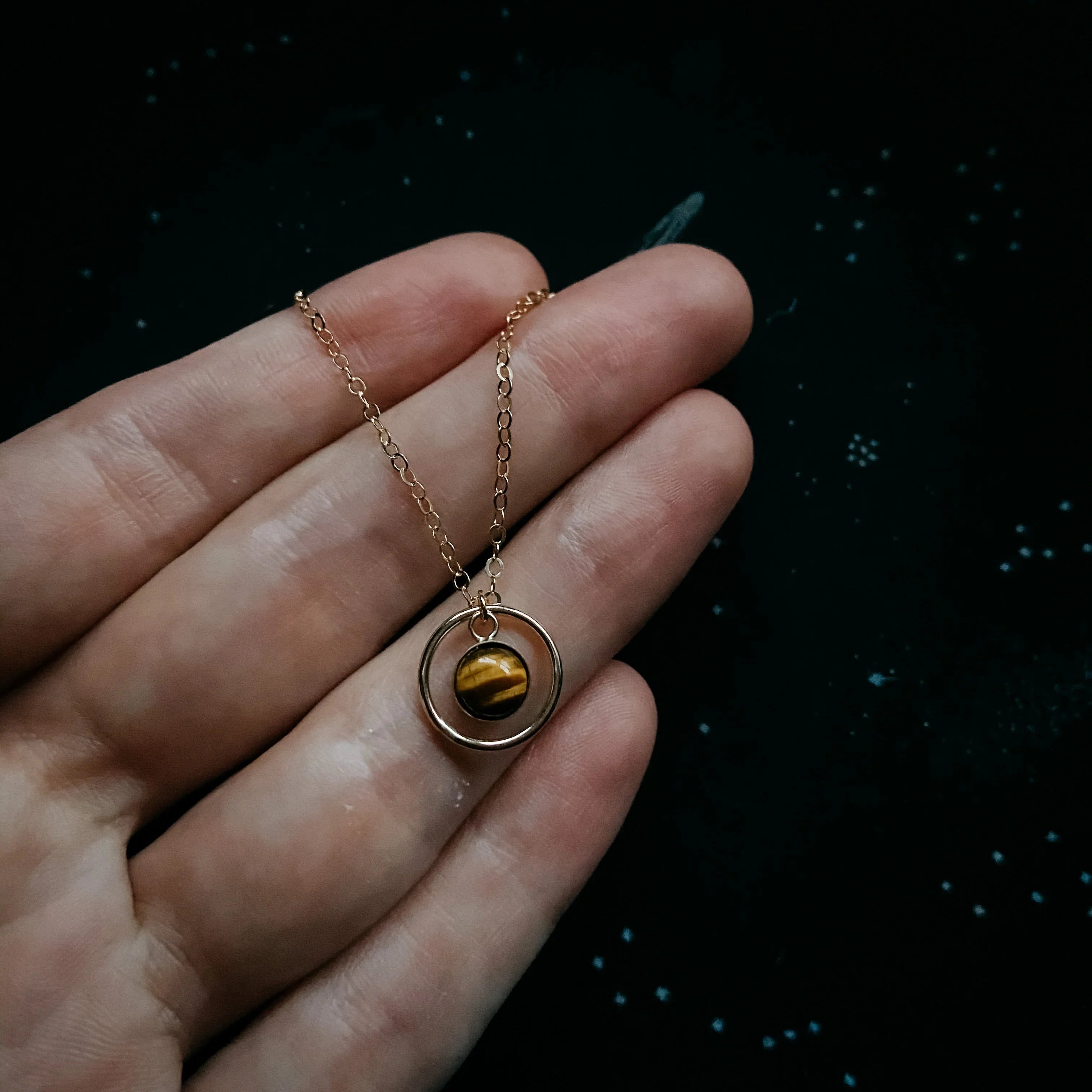 Hand holding cosmic-inspired gold necklace with tiger's eye pendant, Qu!rk Boutique jewelry