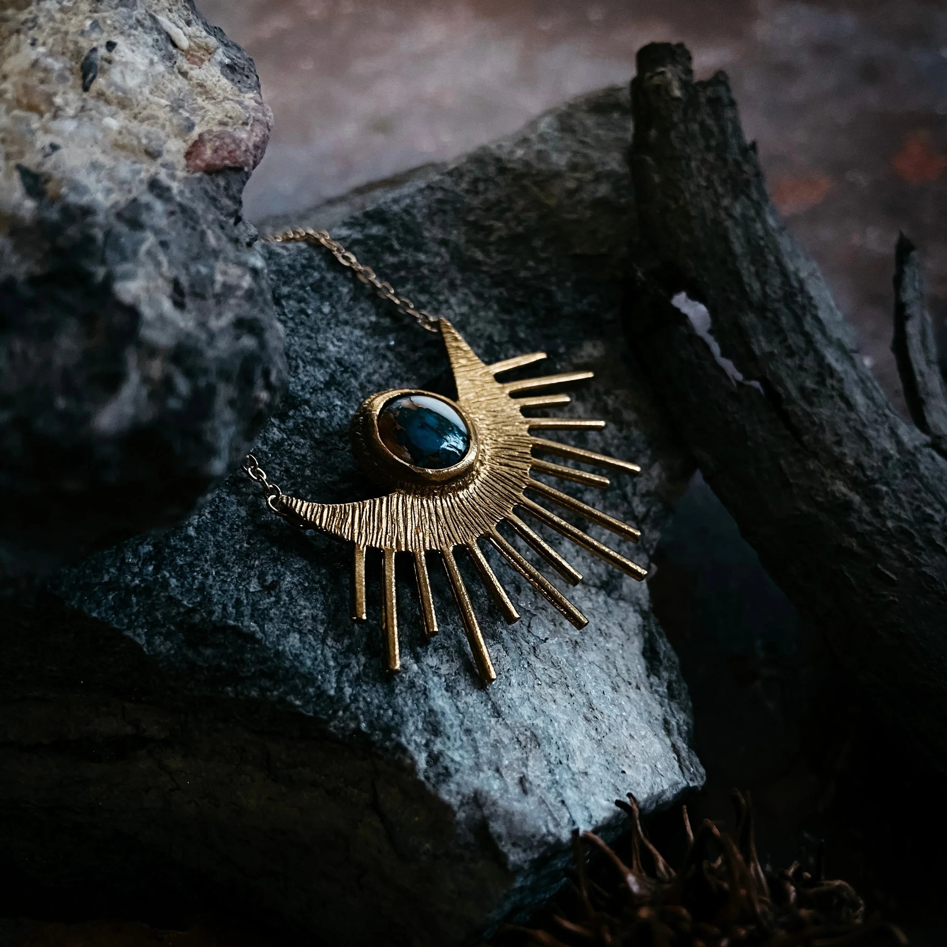 Gold sunburst necklace with blue stone centerpiece on textured dark rocks