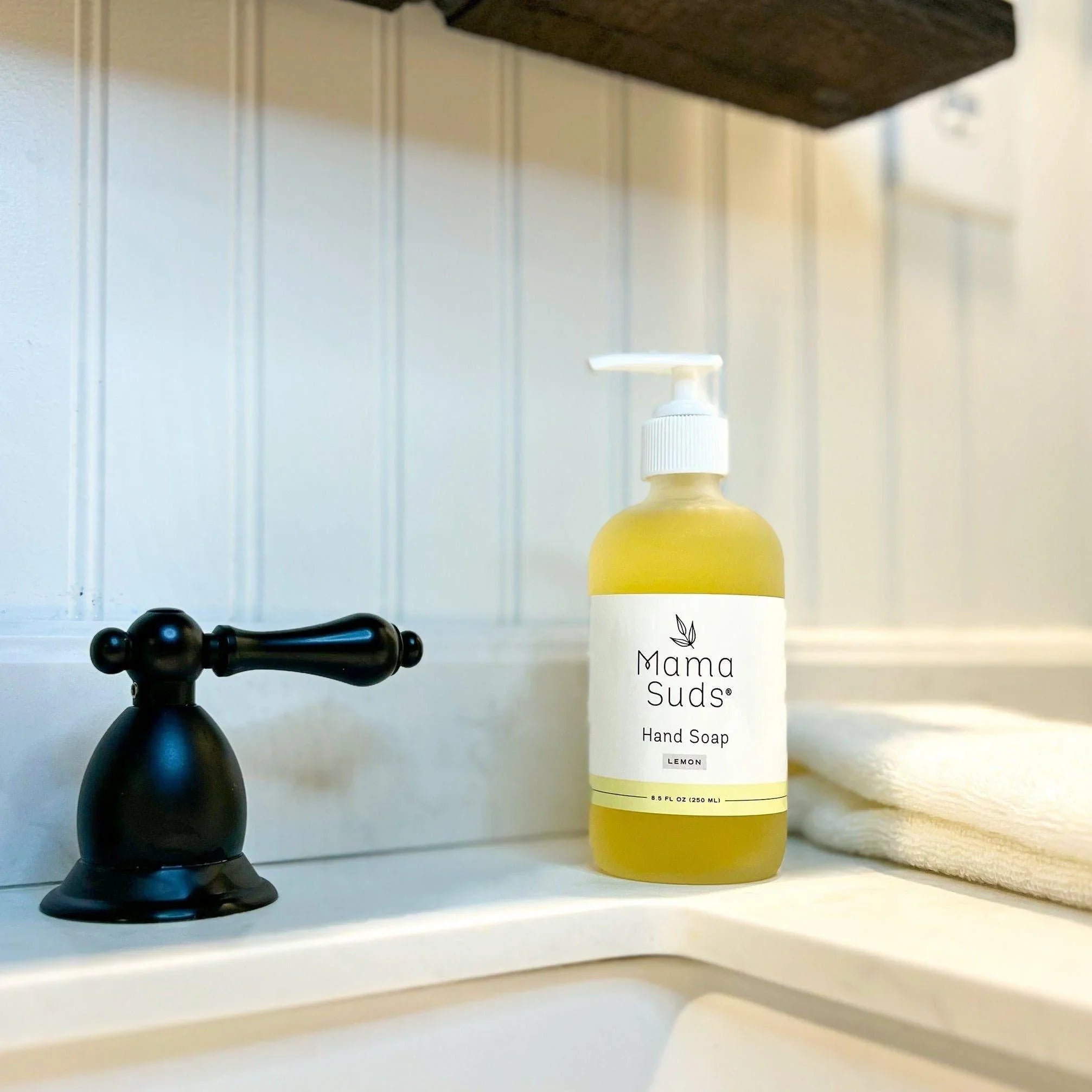 Mama Suds Lemon Hand Soap bottle on a sink beside a black faucet and white towel
