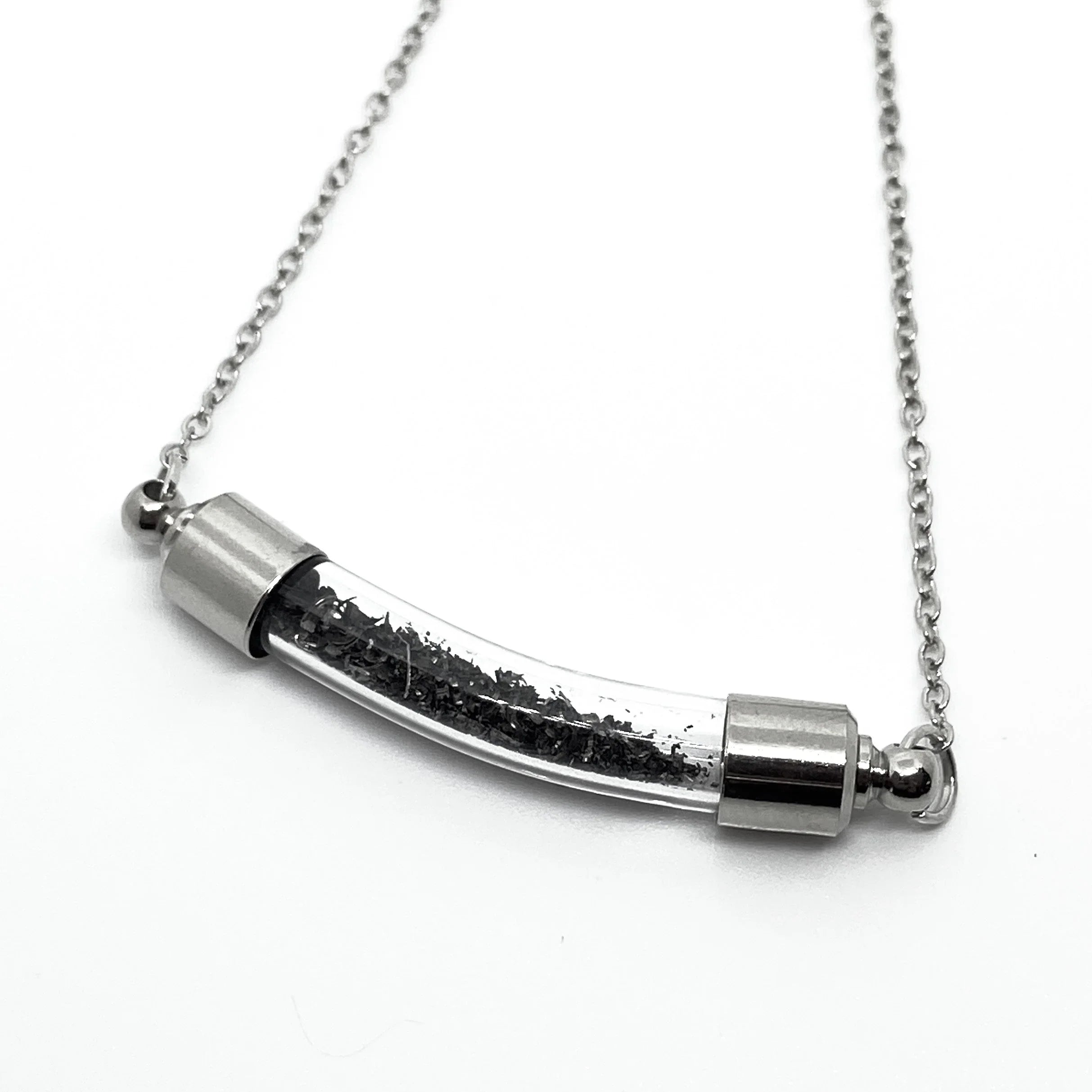 silver chain necklace with curved glass pendant containing small black flakes on white background