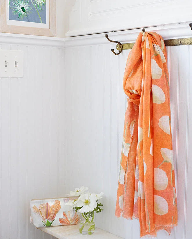 Orange and white polka dot scarf hanging on brass hooks in bright white room with floral pouch and white flowers