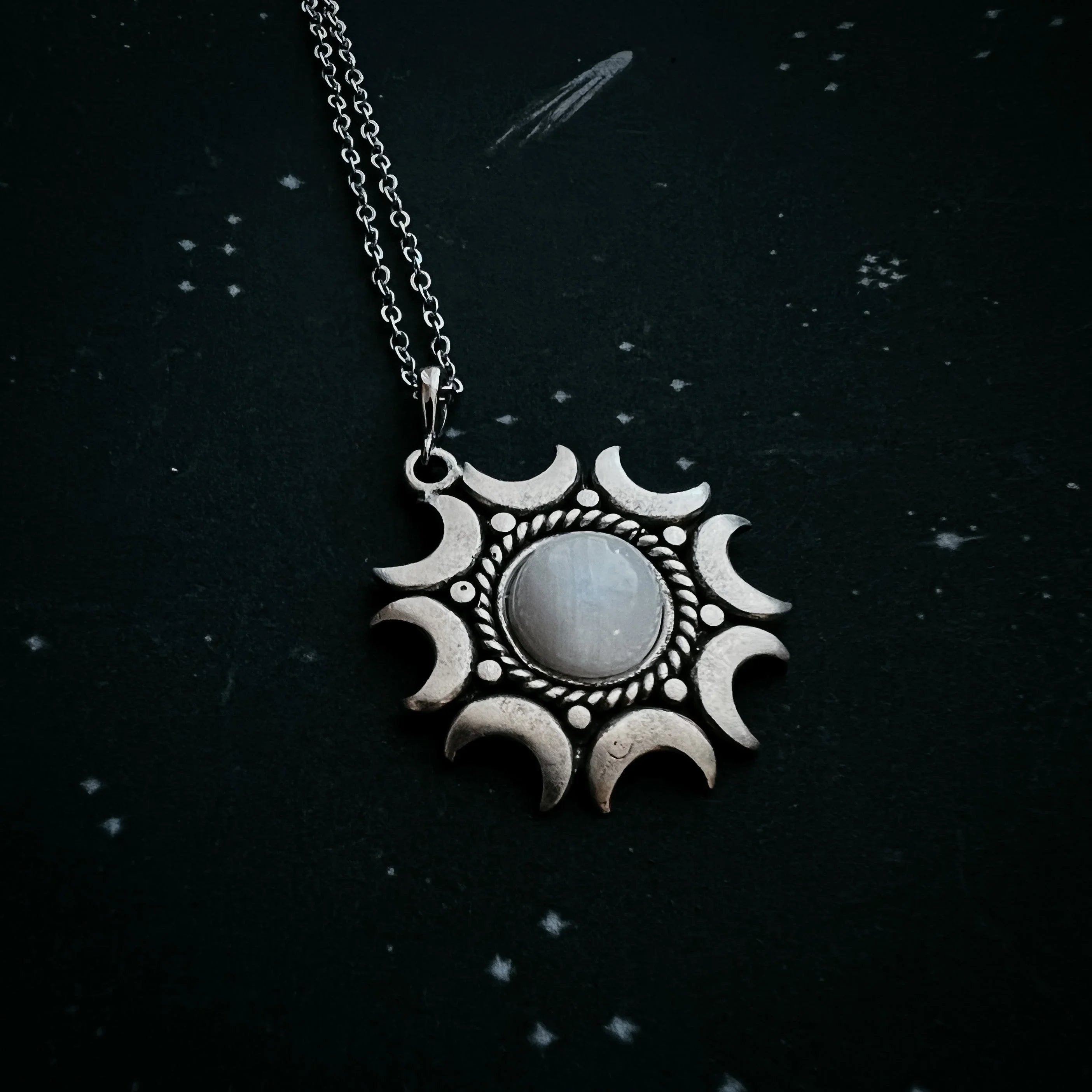 Silver sun and moon phase pendant with central stone on black starry background