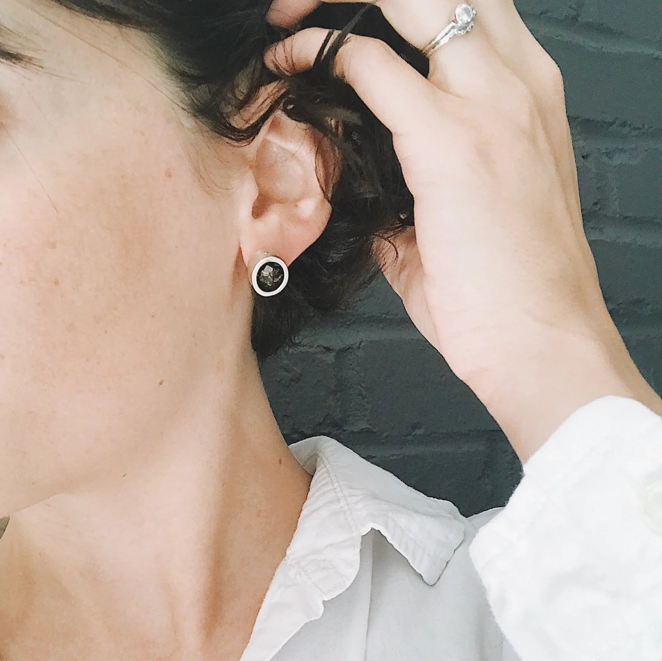 Close-up of a woman wearing silver stud earrings with black stone detail, holding her hair back