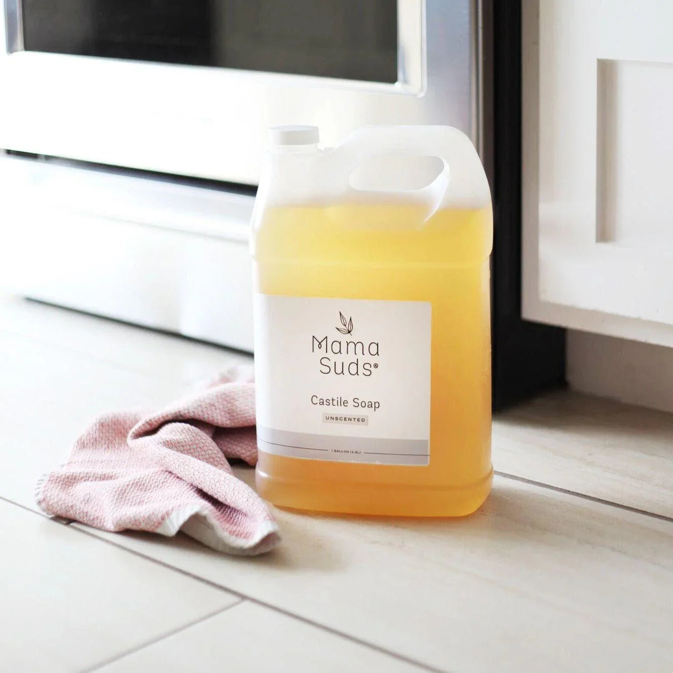 Mama Suds Castile Soap jug with pink cleaning cloth on kitchen floor, eco-friendly gift