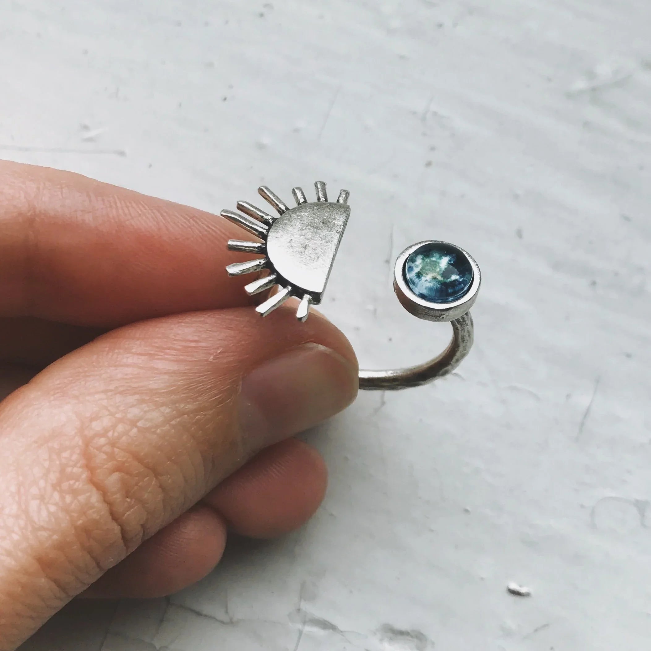 Hand holding silver open ring with sunburst design and blue gemstone, Qu!rk Boutique jewelry