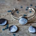 Silver moon phase cuff bracelet with matching moon phase pins on rustic wooden surface