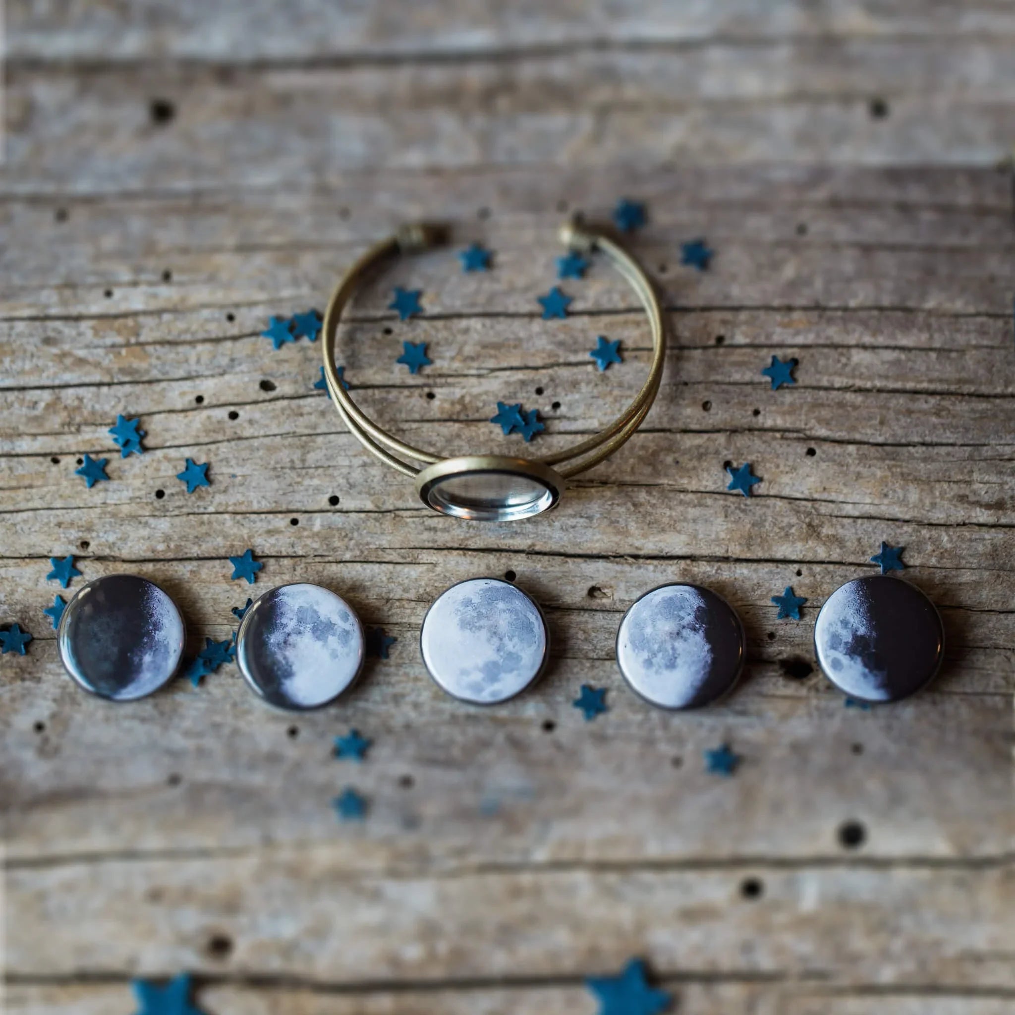 Moon phase jewelry set on rustic wooden surface with scattered blue star confetti