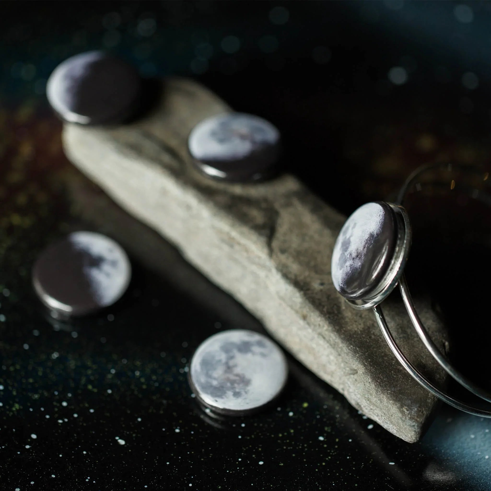Moon phase themed jewelry featuring silver bracelets and round moon stone charms on stone slab