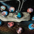 Galaxy-themed round pendant necklace on stone surrounded by colorful nebula-themed cabochons