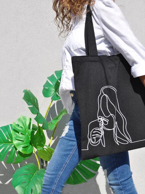 Woman wearing white shirt and jeans carrying black tote bag with minimalist line art of woman holding flower