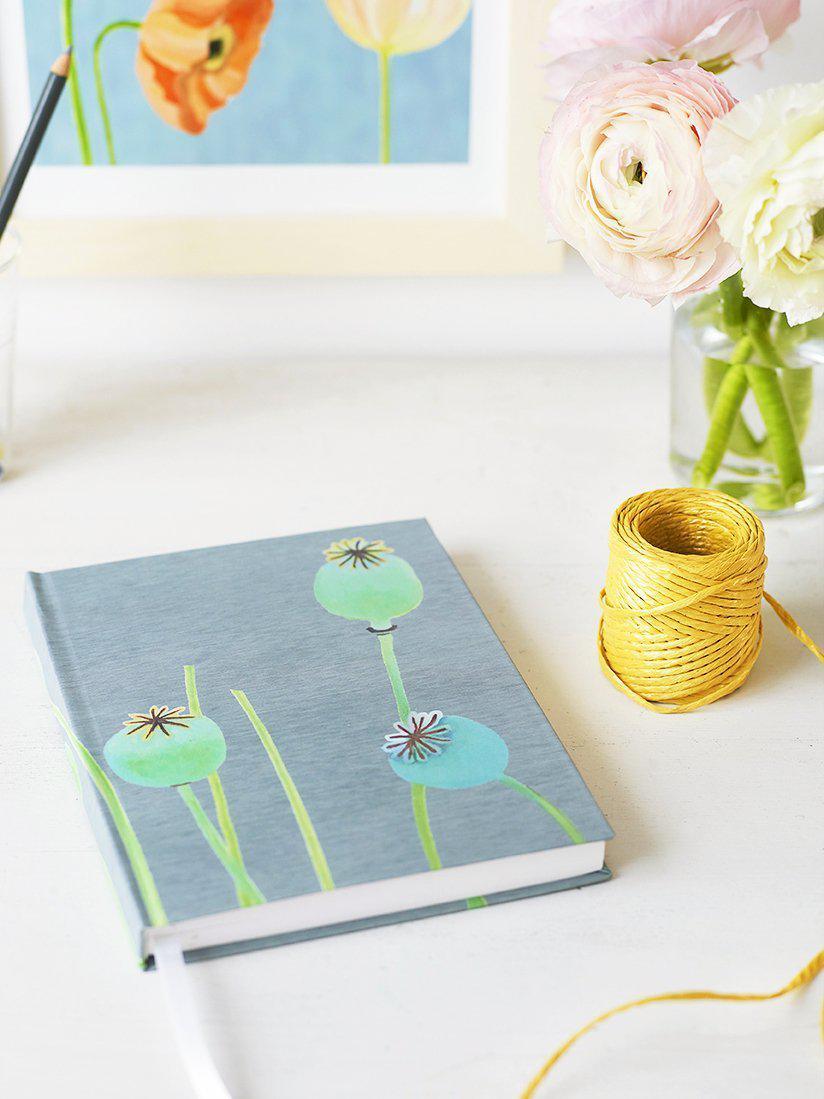 Blue journal with poppy pods illustration on a white table with yellow twine and pink flowers