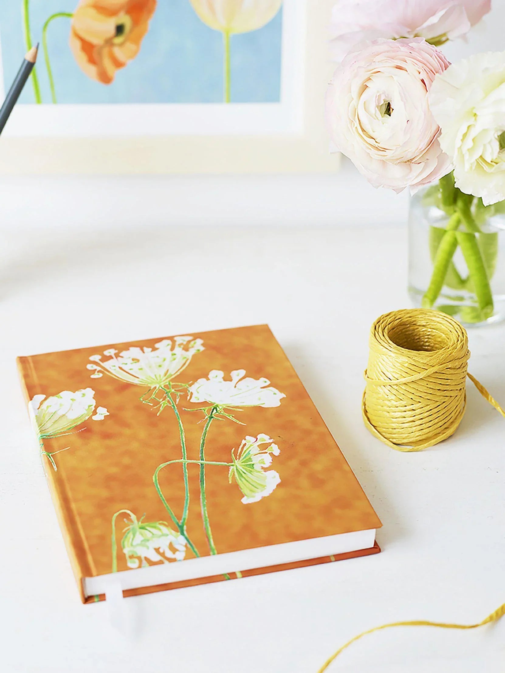 Elegant journal with white Queen Anne's lace flowers on rusty orange cover next to yellow twine and soft pink flowers