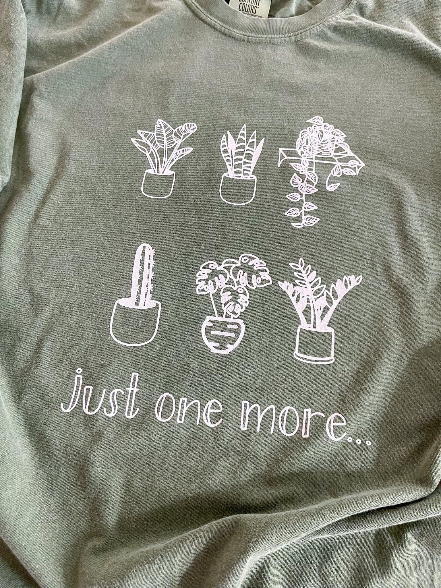 Sage green graphic t-shirt with hand-drawn potted plants and 'just one more...' text