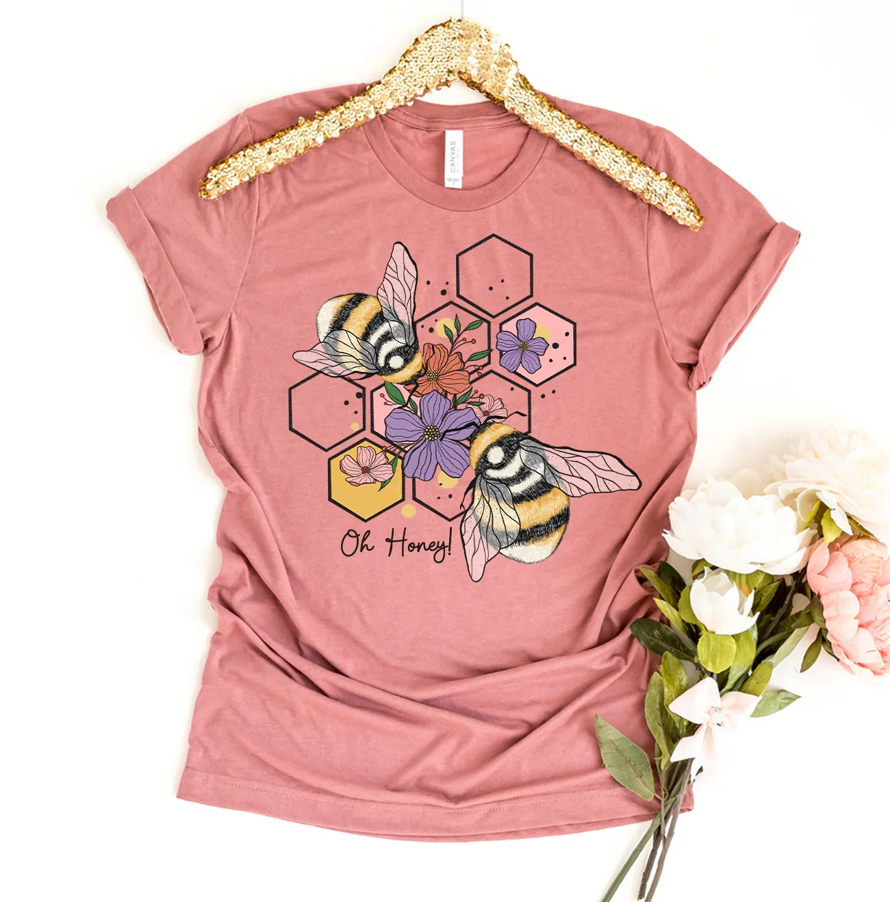 Pink t-shirt with bees, honeycomb, flowers graphic and text Oh Honey, displayed with flowers