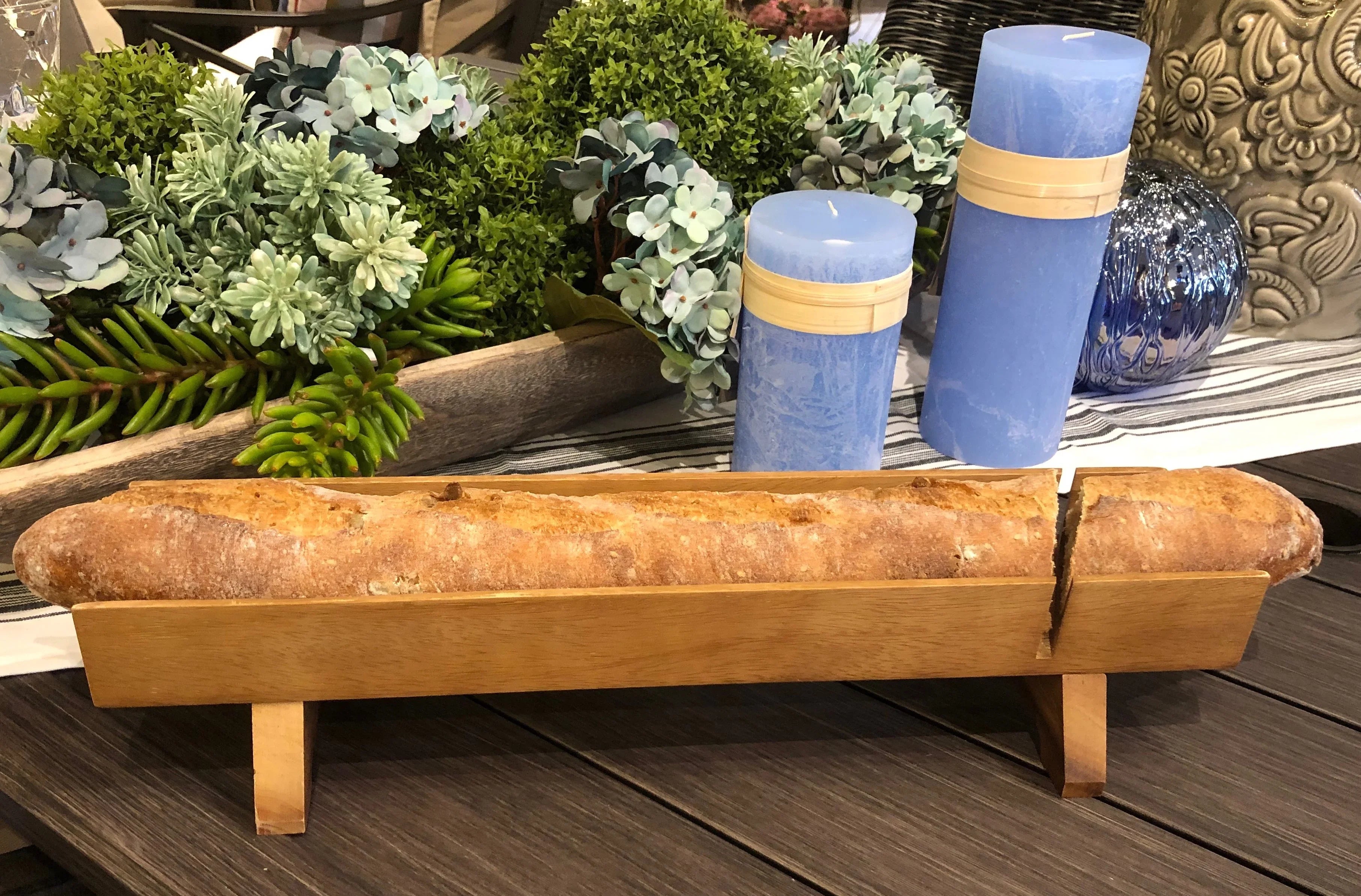 Rustic baguette in wooden tray, blue candles, and faux greenery on boutique display table