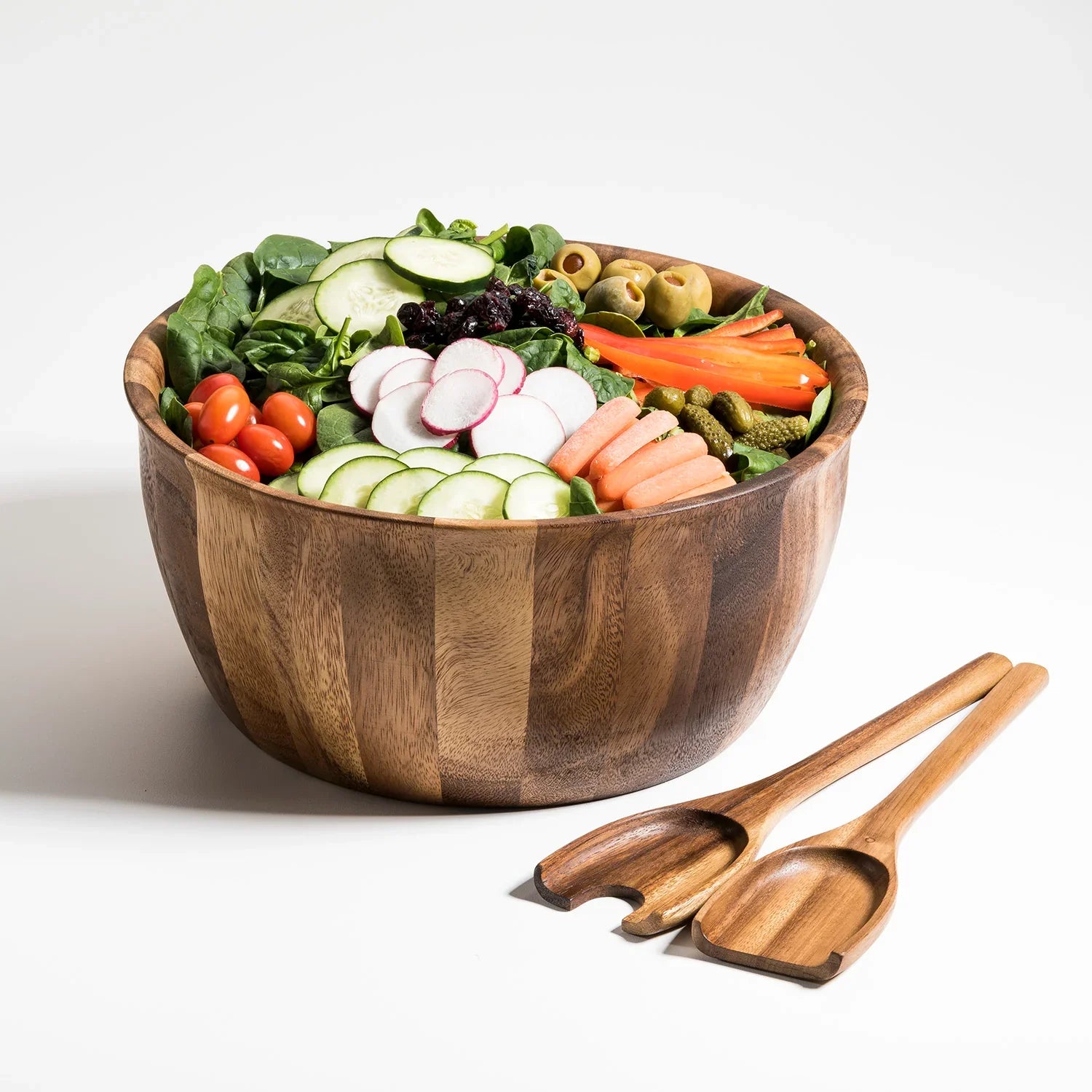 Colorful fresh salad in a wooden bowl with wood salad servers, featuring cucumber, radish, tomato, carrot, olives, and greens. Sustainable kitchenware from Qu!rk Boutique.
