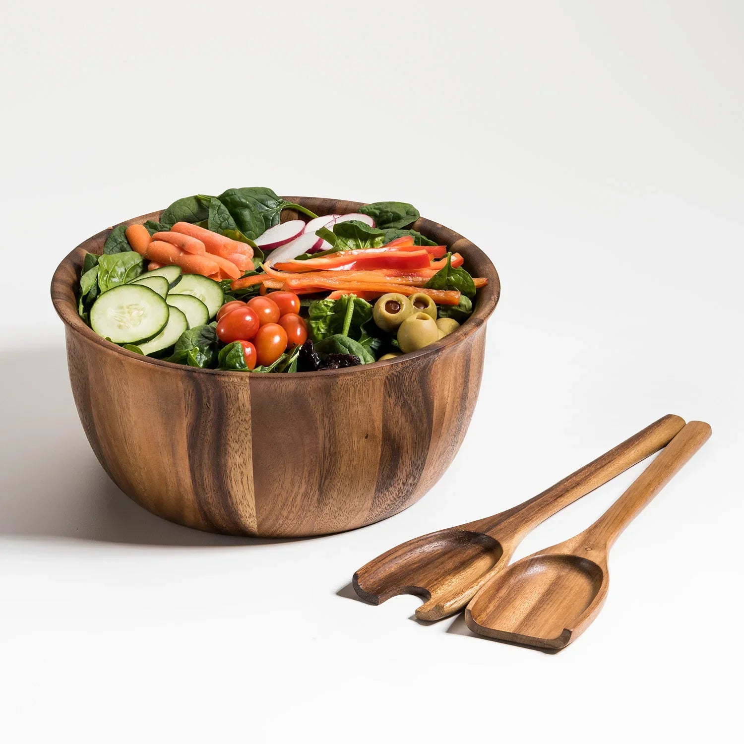 Wooden salad bowl with fresh vegetables, cherry tomatoes, olives, and matching wooden salad servers