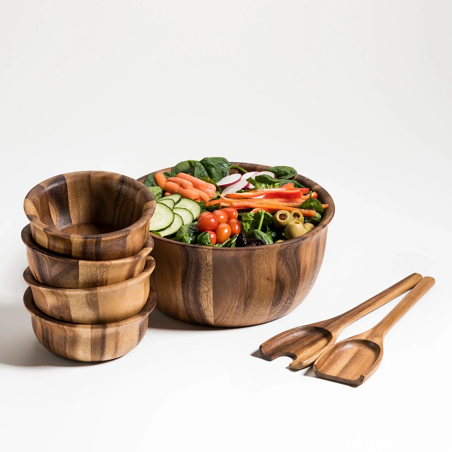Acacia wood salad bowl set with four matching bowls and utensils, filled with fresh vegetables.
