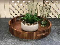 Round wooden serving tray with potted succulent and two green glasses on patio table