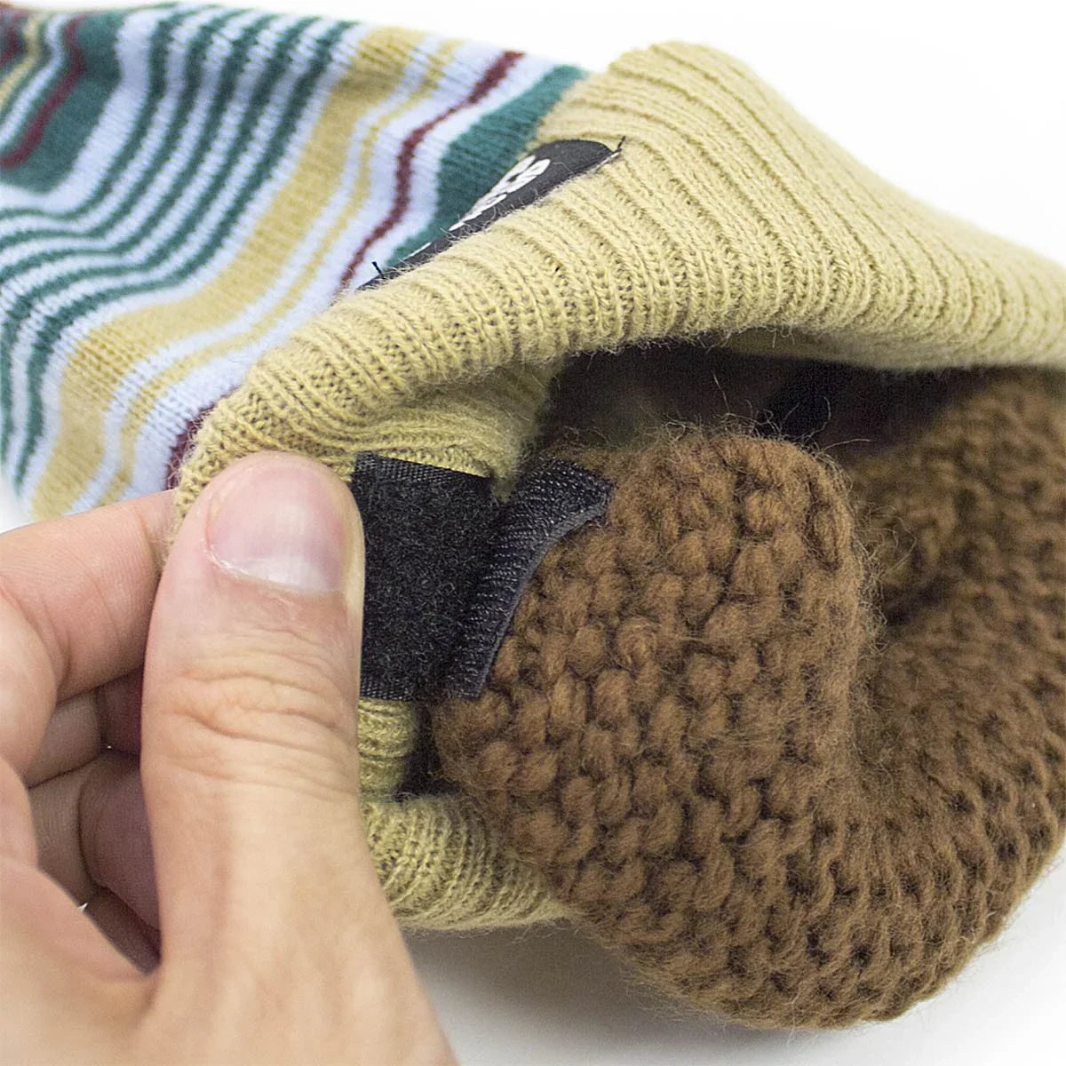 Hand holding a striped wool glove with brown knitted lining and velcro strap attachment
