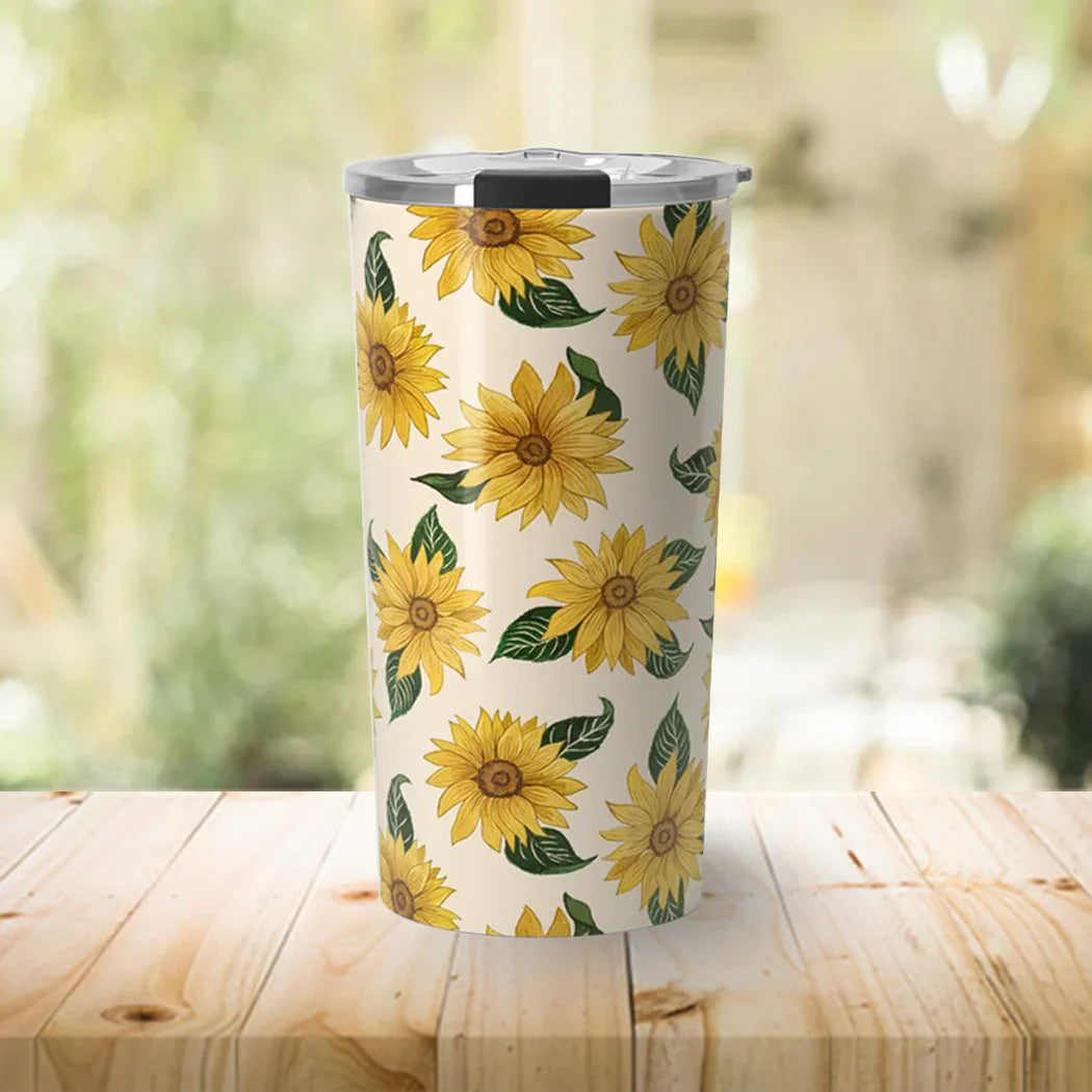 Tall stainless steel tumbler with sunflower and leaf pattern on wooden table in bright room