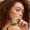 Woman applies Humanist Beauty Herban Wisdom eye cream, promoting natural skincare at Qu!rk Boutique.