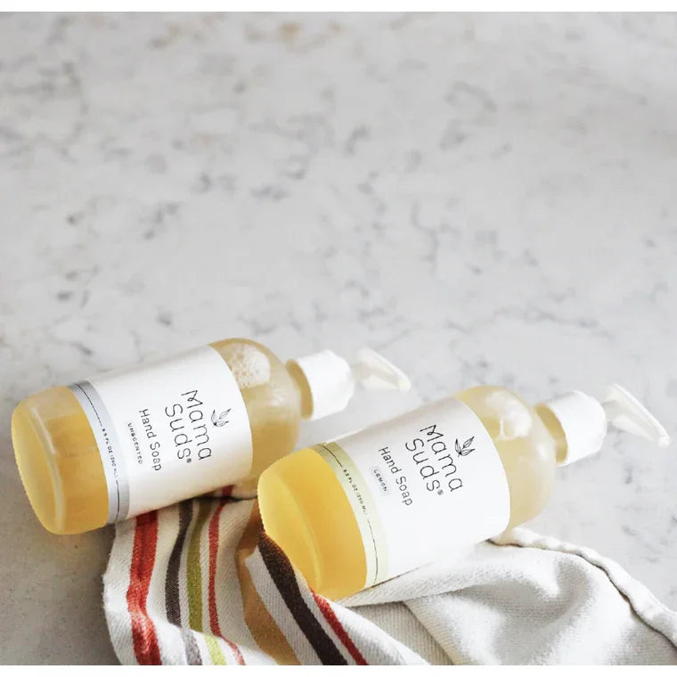 Two bottles of Mama Suds hand soap on a striped cloth, displayed on a light marble counter.