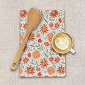 Floral tea towel with orange and red flowers, wooden spatula, and latte on beige fabric