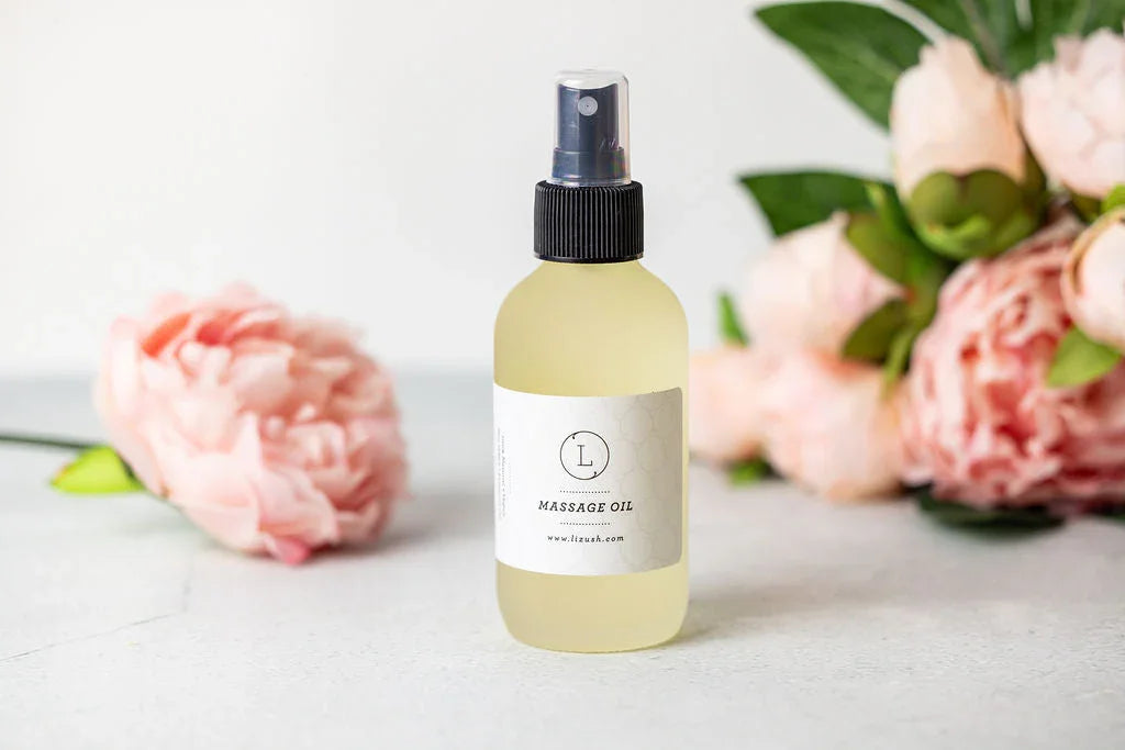 Clear spray bottle of Lizush natural massage oil with pink peonies on white surface