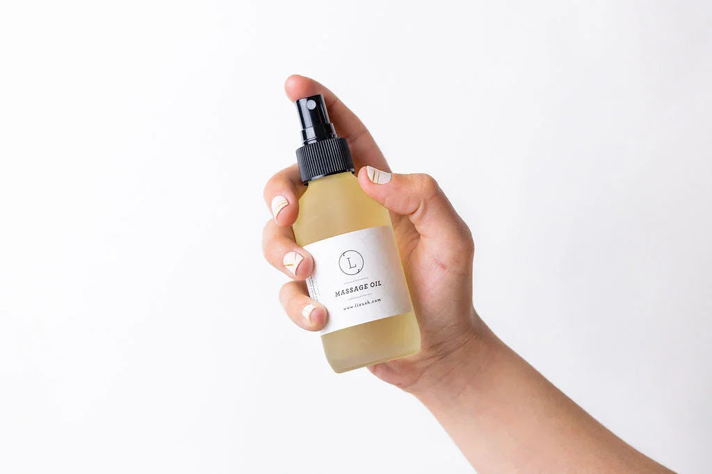 Hand holding a frosted glass spray bottle of massage oil with minimalist white label