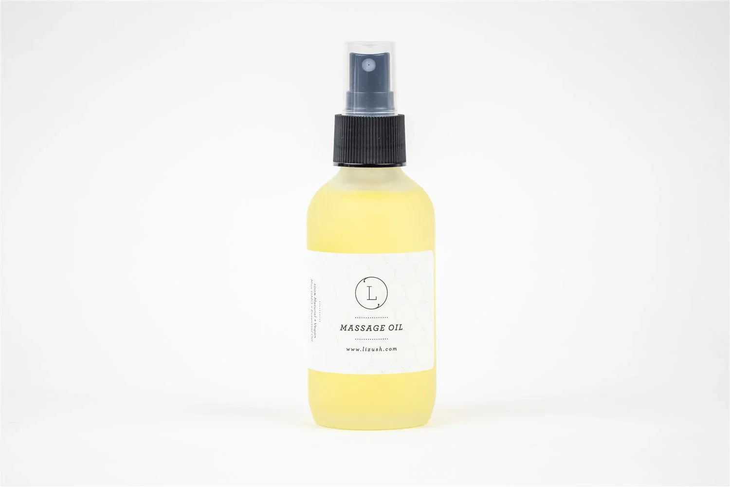 Clear spray bottle of yellow massage oil with white label on white background