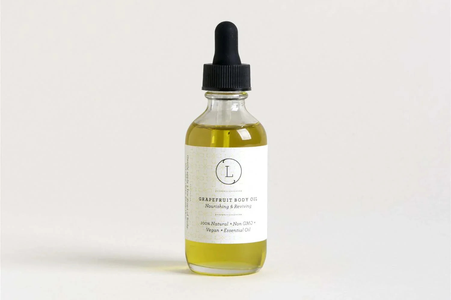 Glass dropper bottle of grapefruit body oil labeled 100% natural, vegan, and essential oil on light background