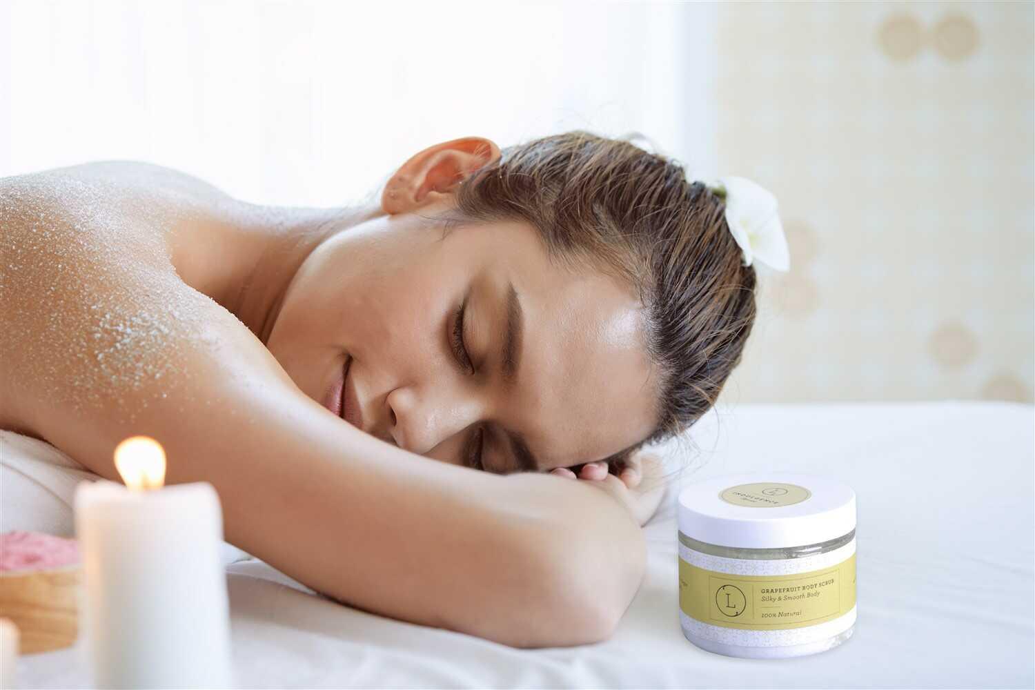 Relaxed woman with grapefruit body scrub on shoulder in spa setting with candle and flower