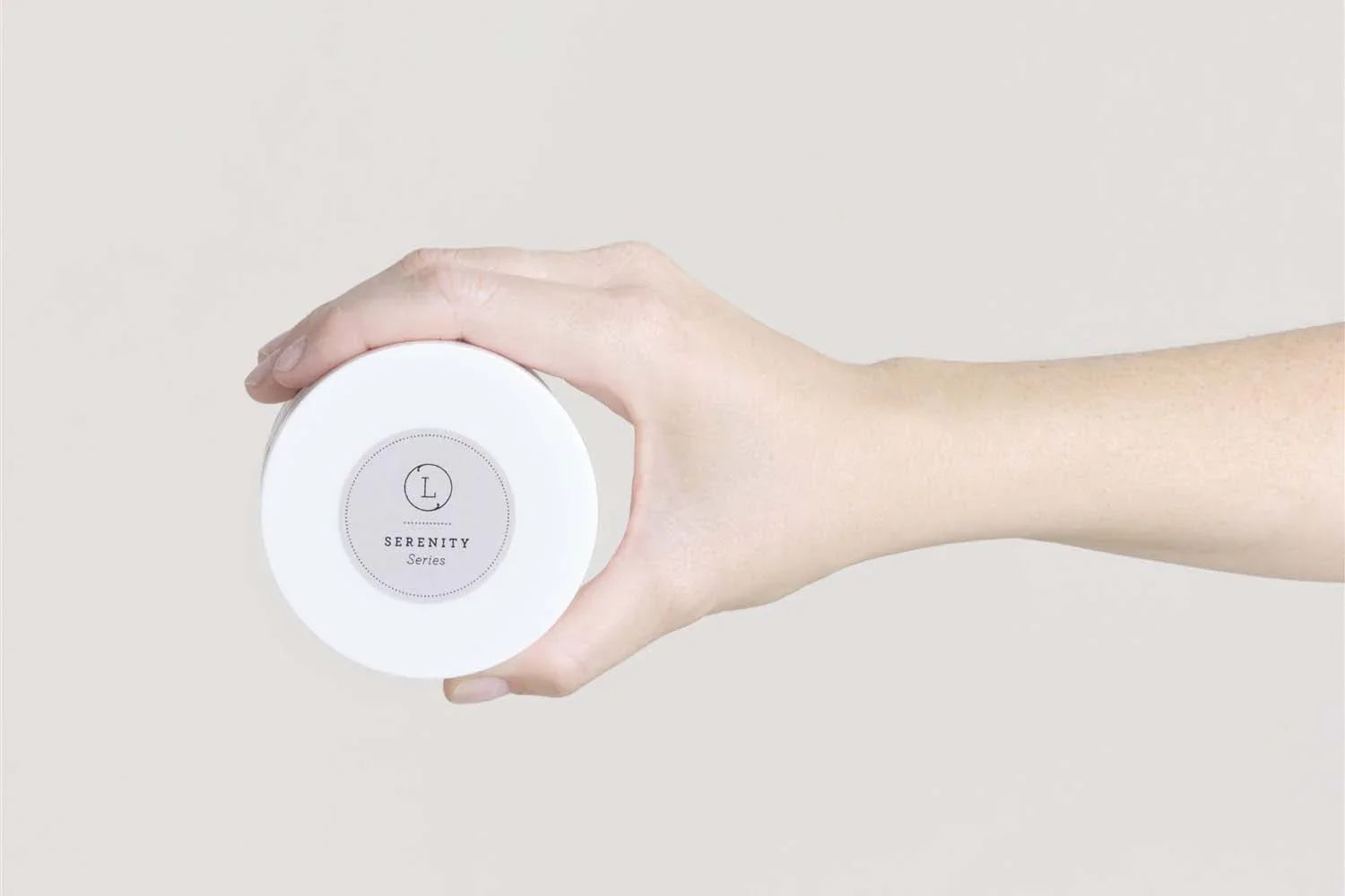 Hand holding white jar labeled Serenity Series natural body scrub in minimalist setting