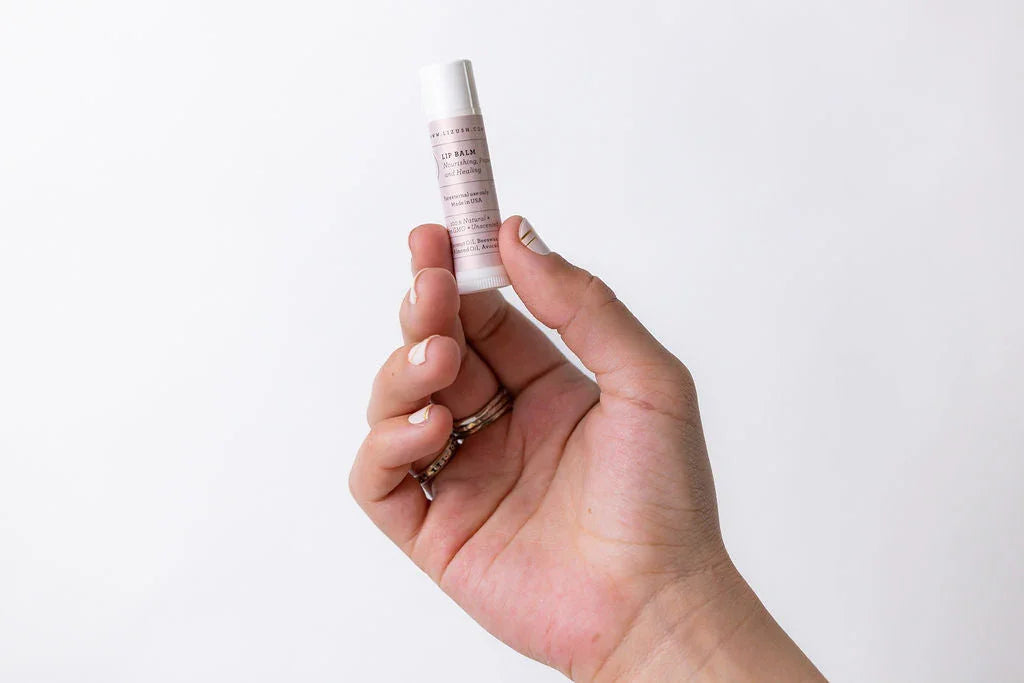Hand holding a natural lip balm stick with a light pink label against a white background