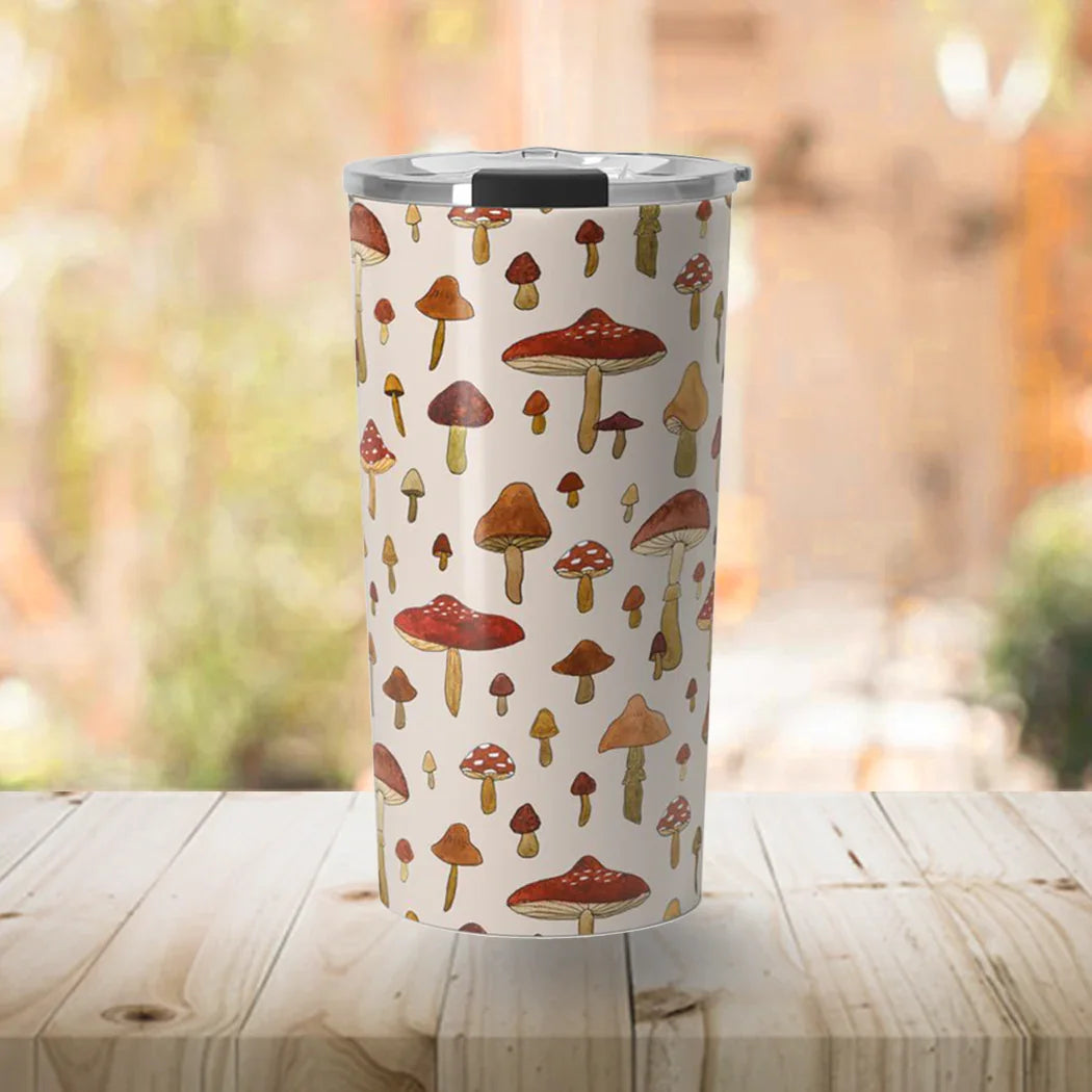 White travel tumbler with colorful mushroom pattern on wooden table with blurred natural background