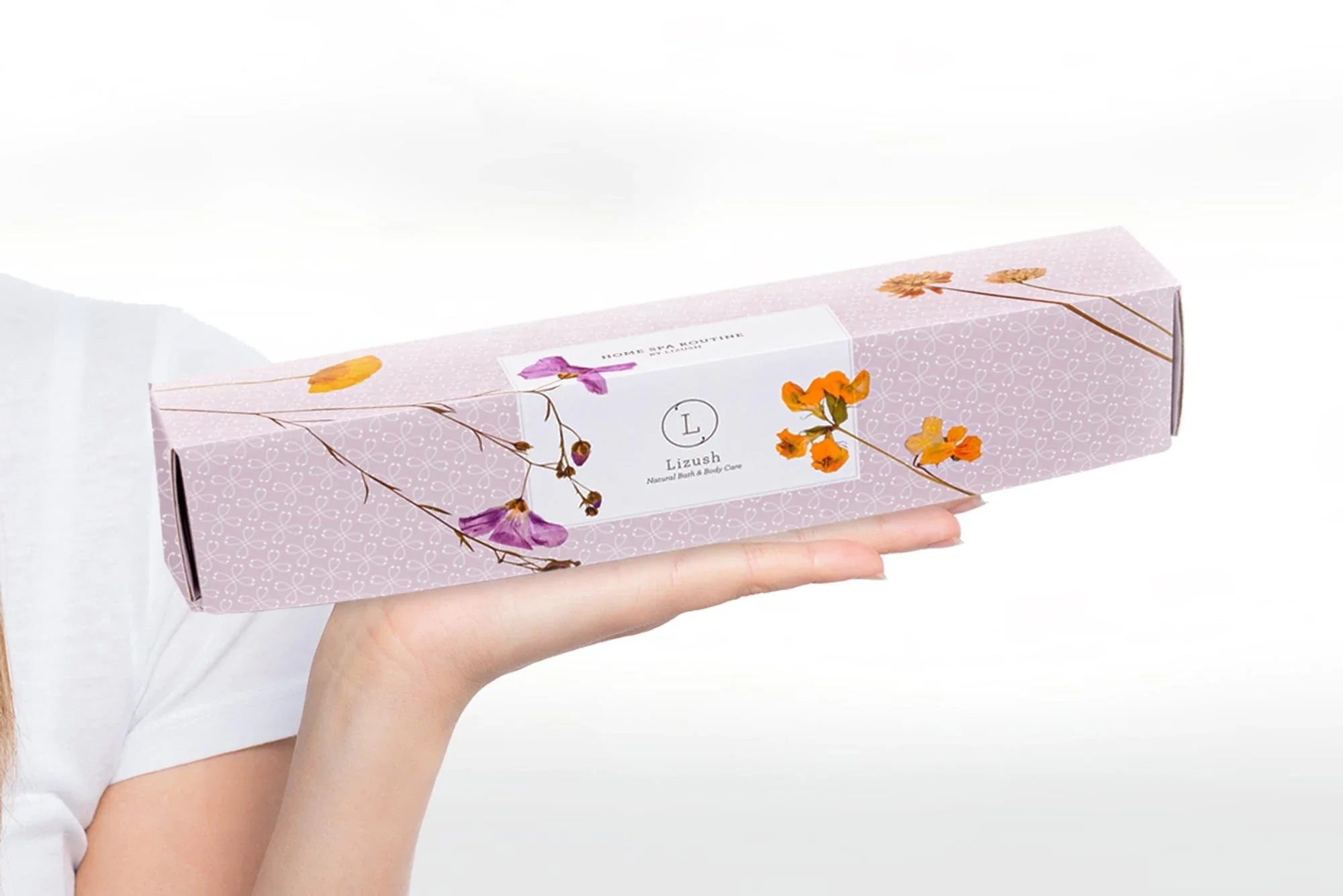 Hand holding a long lavender box with floral design labeled Lizush Home Spa Routine natural bath and body care