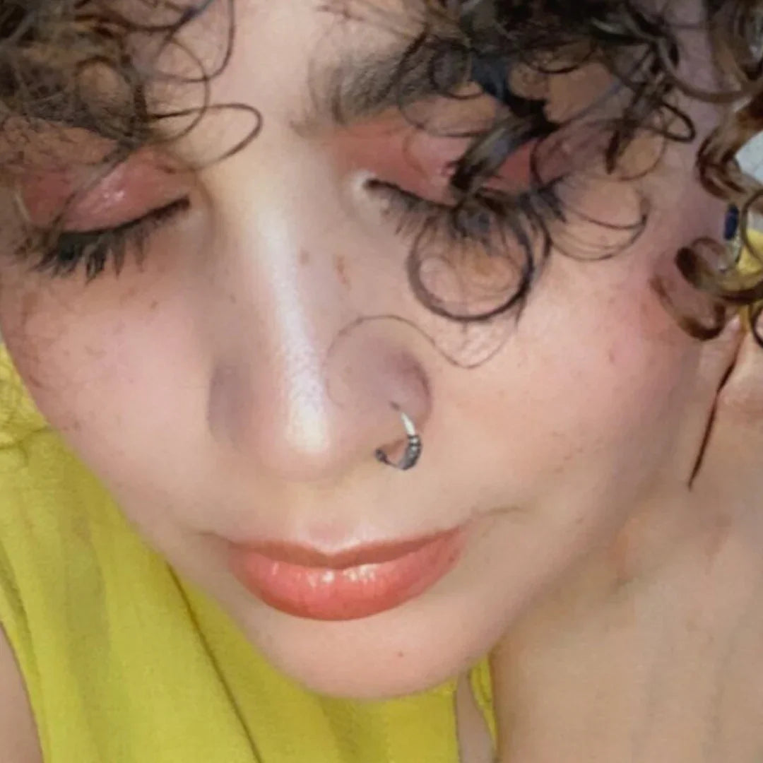 Close-up of a woman with curly hair, a nose ring, soft pink makeup and yellow top, Qu!rk Boutique style.