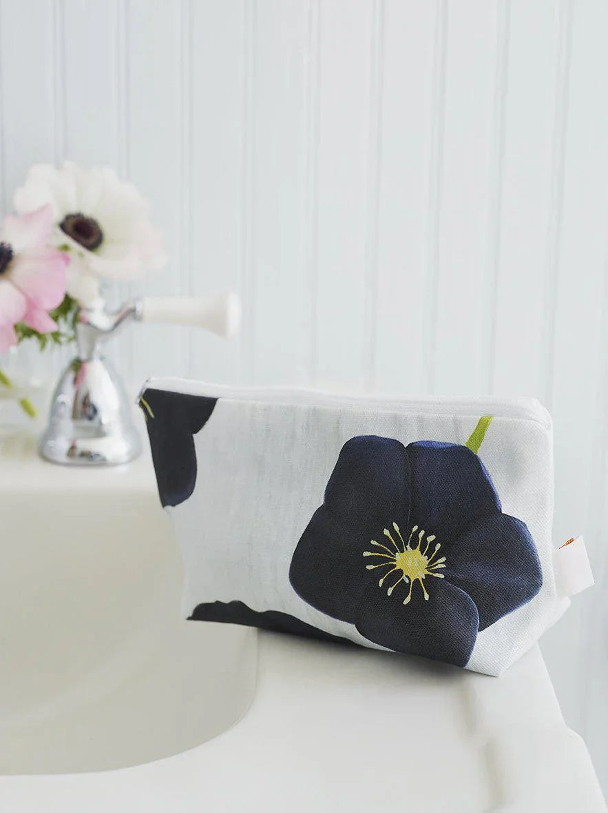 Black flower print makeup bag on white bathroom counter near silver faucet and pink flowers