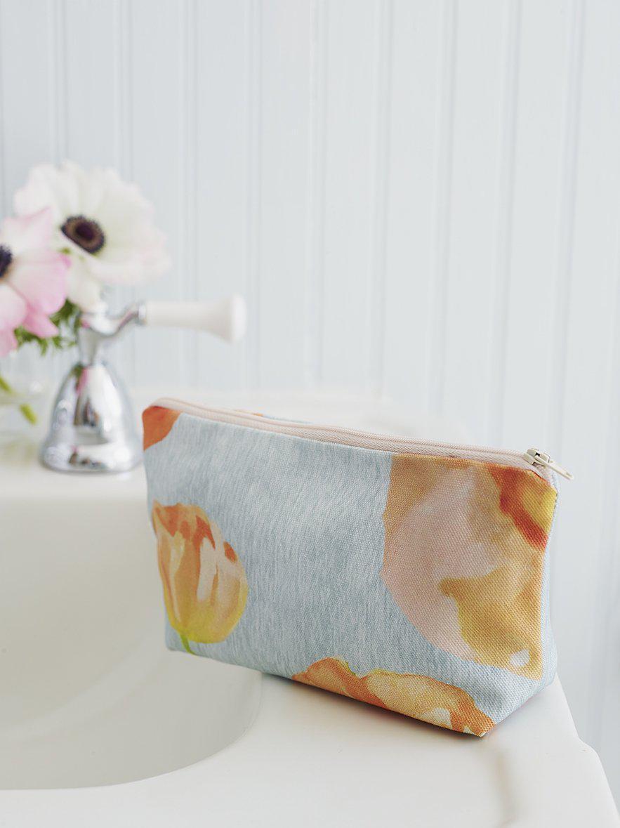 Floral makeup bag with peach poppies design on a white bathroom sink countertop